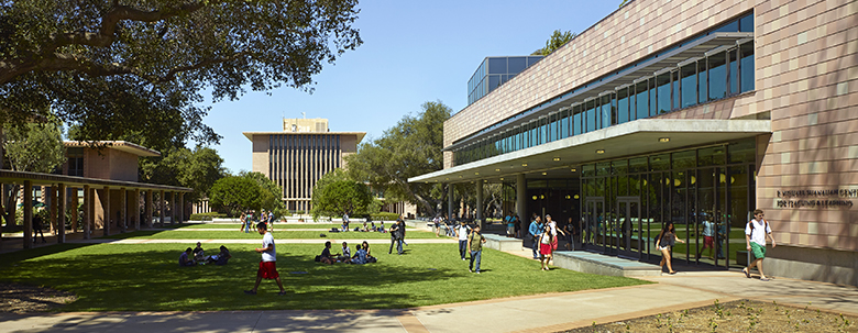 A diverse group of students walking to class and activities are framed by modern buildings on the Harvey Mudd College campus.